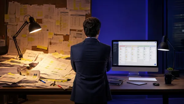 Profissional comparando uma mesa cheia de planilhas com um sistema de CRM organizado na tela do computador.